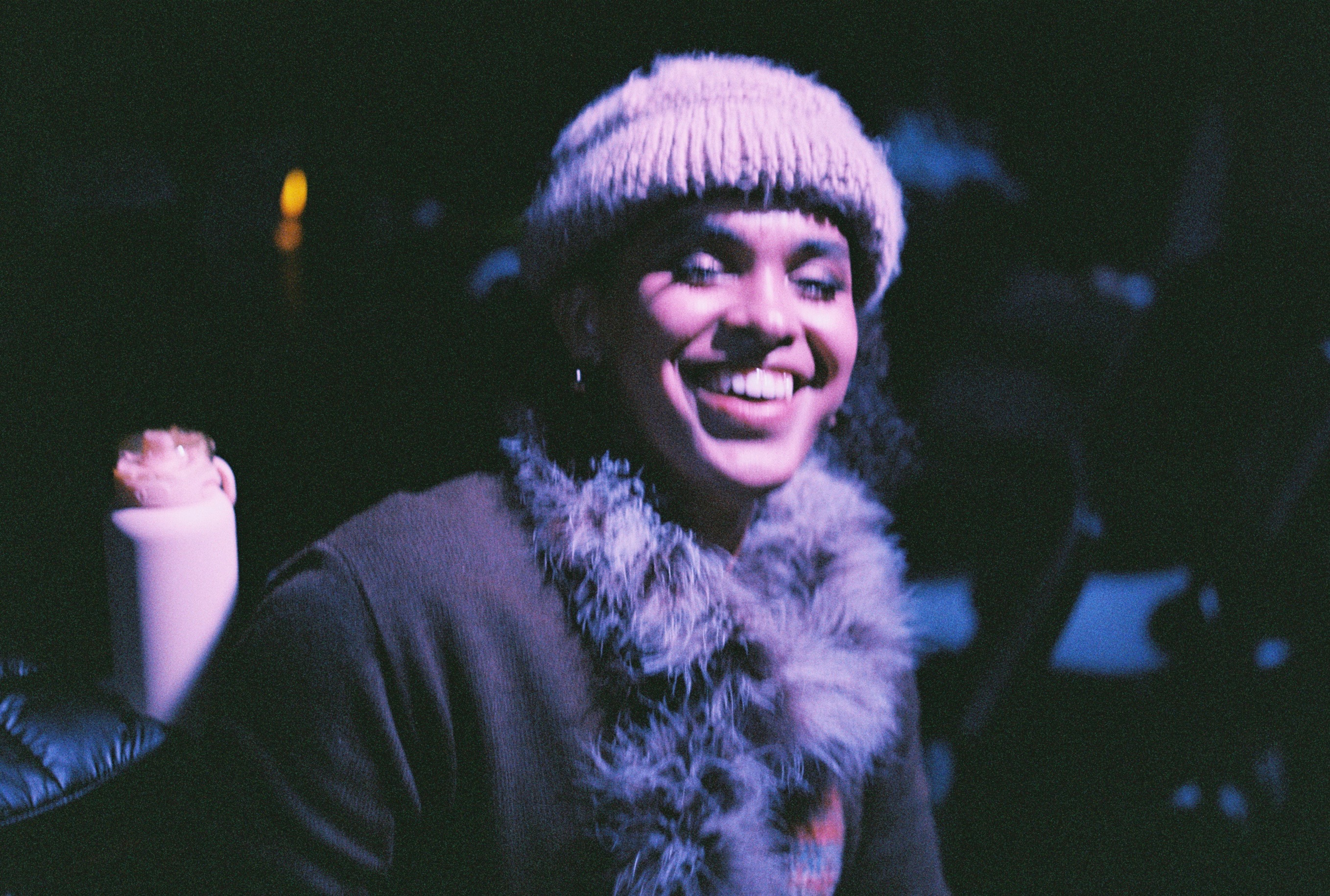 Rafi smiling warmly, wearing a beanie and textured coat in an artistic purple-tinted photograph